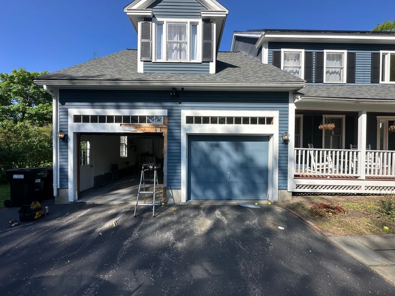 Dual white garage doors with transom windows being installed on blue colonial home