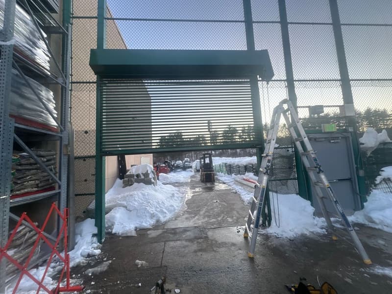 Green commercial rollup door at garden center loading area in winter with snow